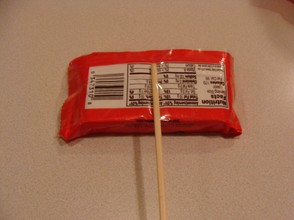 Tape the stick to the back of the candy.