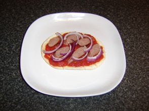 The sliced sausage and onion are added to the pizza
