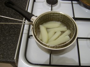 Chips are parboiled in a wire basket in water